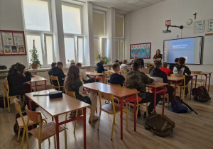 W sali w ławkach siedzą uczniowie. W głębi kadru widać przedstawicieli Straży Miejskiej prowadzących zajęcia.