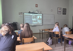Uczniowie siedzą w klasie w ławkach. Na tablicy multimedialnej widać lekcję online z Centrum Nauki Kopernik
