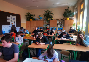 W sali lekcyjnej uczniowie siedzą w ławkach. W rękach trzymają telefony i rozwiązują quiz geograficzny.