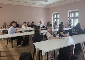 Uczniowie siedzą w ławkach w pomieszczeniu