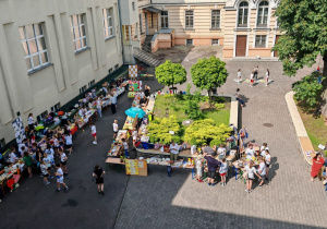Widok dziedzińca szkolnego z góry. Na dziedzińcu widać stoiska oraz dzieci chodzące między stoiskami