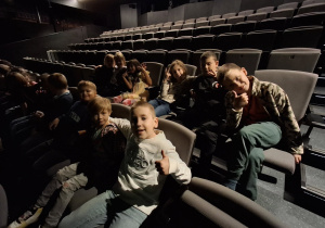 Uczniowie siedzą na fotelach w sali teatralnej.