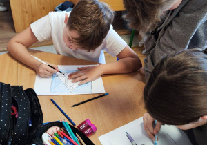 Przy ławce siedzi trójka uczniów. Rozwiązują zadania konkursowe.