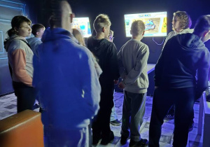 W pomieszczeniu oświetlonym niebieskim światłem stoją dzieci i oglądają wystawę.