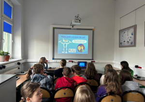 W klasie przed tablicą multimedialną siedza uczniowie. Oglądają prezentację na temat bezpiecznego internetu.