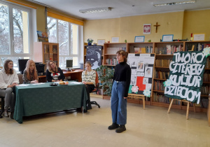 W pomieszczeniu stoi uczennica naszej szkoły. Po lewej stronie zdjęcia widać jury konkursowe.