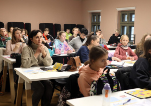 W pomieszczeniu przy stolikach siedzą uczniowie wraz z opiekunami