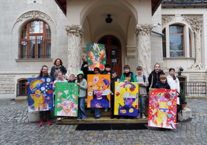 Na schodach Willi pod Jabłoniami stoi grupa uczestników projektu. Pięć osób trzyma plakaty, które uczestnicy wykonali podczas spotkania.