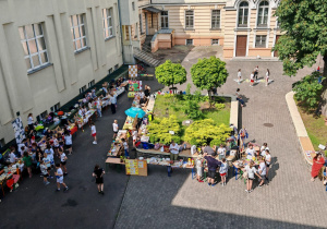 Widok dziedzińca szkolnego z góry. Na dziedzińcu widać stoiska oraz dzieci chodzące między stoiskami