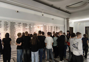 W holu sejmowym stoją uczniowie, oglądają tablicę pamiątkową