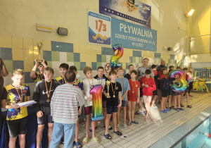 Na pływalni stoją dzieci wraz z trenerami. Widać cyferki 1, 2 i 3.