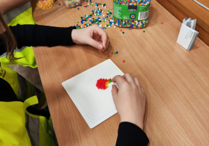 Zdjęcie przedstawia ręce osoby układającej koraliki do prasowania na specjalnej podkładce.