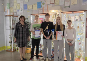 Na szkolnym korytarzu na tle gablot z pucharami stoi pani dyrektor wraz z przedstawicielami drużyn pływackich.