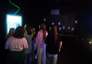 W pomieszczeniu z dwoma ekranami multimedialnymi stoi grupa uczniów.