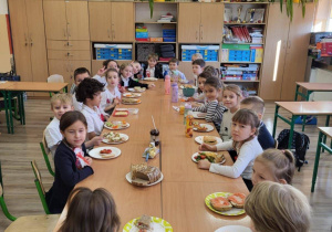Przy dużym stole siedzą uczniowie przy wspólnym śniadaniu