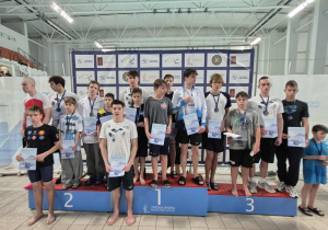 Na stopniach podium stoją zawodnicy biorący udział w zawodach. Widać siedemnastu chłopców.