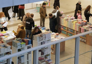 Zdjęcie z góry przedstawia fragment hali dworca Łódź Fabryczna. Widać stragany z książkami oraz ludzi odwiedzających targi.