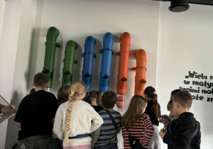 W pomieszczeniu stoją uczniowie, przyglądają się kolorowym rurom
