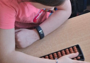 Na zdjęciu widać dziewczynkę pochyloną nad liczydłem leżącym na stole