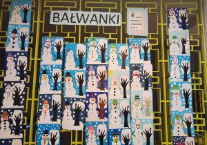 Na kracie na korytarzu szkolnym wiszą prace uczniów. Wykonali oni bałwanki z papieru.