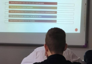 W ławce siedzi uczeń. Ogląda prezentację na temat ochrony danych osobowych wyświetloną na tablicy
