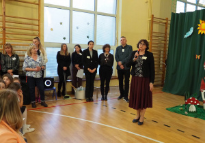 Na sali gimnastycznej do rodziców przemawia pani dyrektor. Tuż za panią dyrektor stoją nauczyciele i pracownicy szkoły.