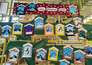 Na korytarzu szkolnym na kracie wiszą prace uczniów wykonane na lekcji techniki. Są to karmniki wykonane z papieru. W środku każdego karmnika widać ptaszki różnych gatunków.