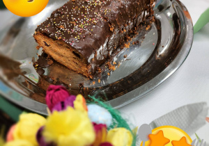 Na stole przykrytym białym obrusem stoi srebrna taca, na której leży ciasto.