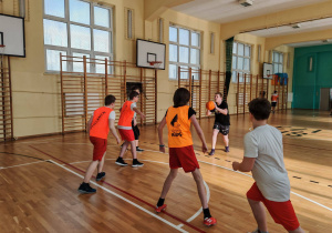 W sali gimnastycznej sześciu chłopców gra w koszykówkę.