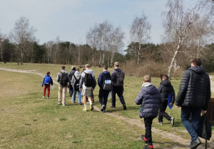 Ścieżką wśród zieleni idzie grupa uczniów wraz z opiekunami.