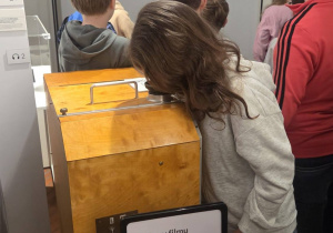 W sali muzeum uczniowie oglądają eksponaty na wystawie.