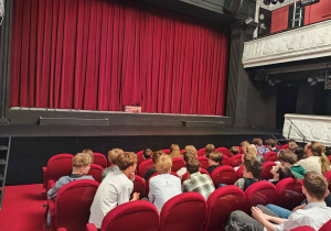 W sali teatralnej na fotelach siedzą uczniowie.