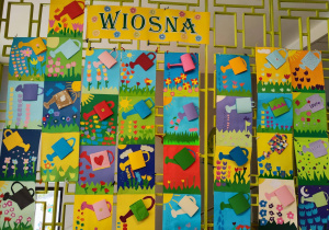 Na kracie wiszą prace plastyczne wykonane przez dzieci. Są to konewki papierowe przyklejone na karton.