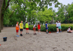 W parku uczniowie ubrani w stroje sportowe przygotowują się do startu w biegu.