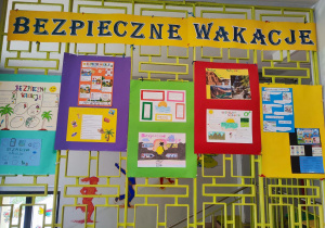 Na korytarzu szkolnym na kracie wiszą plakaty dotyczące bezpiecznego spędzania wakacji