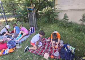 Na trawie na rozłożonych kocach siedzą dzieci.