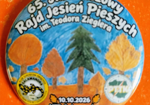 Na zdjęciu widać okrągłą przypinkę z nazwą rajdu i rysunkami drzew