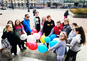 grupa naszych uczniów stoi na placu Wolności pozując do zdjęcia z balonami