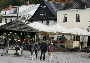 Zdjęcie przedstawia rynek Kazimierza Dolnego, na środku rynku znajduje się stara studnia, z którą związana jest legenda miasta. Po rynku spacerują turyści.