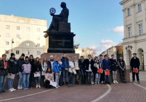 Uczniowie stoją pod pomnikiem Mikołaja Kopernika, pozując do zdjęcia grupowego.