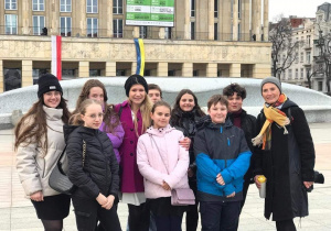 grupa uczniów klasy 7c wraz z dwojgiem opiekunów stoi przed Teatrem Wielkim na placu Dąbrowskiego