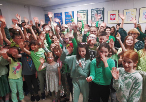 duża grupa uczniów z różnych klas stoi na korytarzu szkolnym, są ubrani w zielone koszulki, wszyscy machają do oglądających zdjęcie