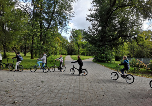 na zdjęciu widać uczniów jeżdżących na rowerach po alejkach parkowych