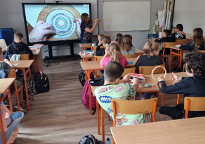 dzieci na lekcji siedzą w klasie, słuchają i oglądają instrukcję jak należy pracować z okrągłym krosnem