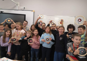 grupa dzieci prezentuje efekty pracy na zajęciach techniki, wszyscy trzymają okrągłe krosna z utkanymi serwetkami