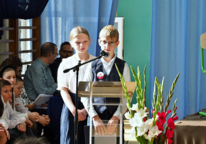 na zdjęciu uczniowie stoją przy mikrofonie i przytaczają słowa uczniów o szkole
