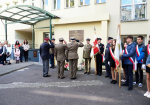 żołnierze salutując oddają hołd żołnierzom upamiętnionym na tablicy pamiątkowej, obok stoi poczet sztandarowy szkoły