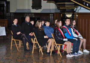 uczniowie pocztu sztandarowego siedzą w kościele na krzesełkach