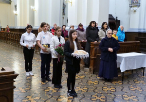 uczniowie stoją trzymając dary ołtarza, w tle pani dyrektor wraz z delegacją z Ukrainy