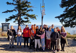 grupa uczniów klasy 8d wraz z wychowawcą stoi na górze pod tabliczką z napisem "Barania Góra"